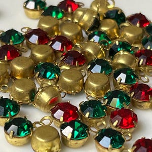 May include: A collection of small, round, faceted rhinestones set in brass-toned metal casings. Each individual piece features a single loop for attachment, alternating between vibrant emerald green and deep ruby red coloured stones.