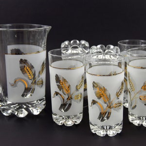 Könnte beinhalten: Ein Set aus sechs gefrosteten Gläsern mit Blattgold-Akzenten. Die Gläser haben eine weiße, gefrostete Oberfläche mit einem Blattgold-Design aus Blättern und Weizen. Das Set enthält auch einen passenden Krug.