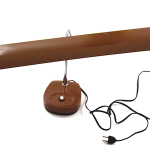 May include: A brown desk lamp with a long, rectangular shade and a round base. The lamp has a flexible arm and a black cord with a plug.