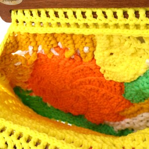 Pu&ograve; includere: Un pezzo all'uncinetto fatto a mano, colorato, con un vivace mix di filati gialli, arancioni, verdi e bianchi. Il pezzo &egrave; sospeso a un telaio di legno, mostrando un design strutturato e a trama aperta. L'estetica generale ricorda l'artigianato vintage.
