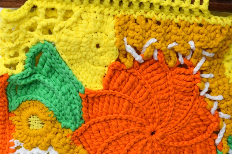 Pu&ograve; includere: Primo piano di un colorato pezzo all'uncinetto fatto a mano. Il design presenta grandi motivi floreali strutturati nelle tonalit&agrave; del giallo, dell'arancione e del verde. Le cuciture bianche accentuano i bordi, creando un tessuto vibrante e tattile.