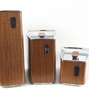 May include: Set of three wooden canisters with chrome lids. The canisters are labelled "S", "C", and "T".