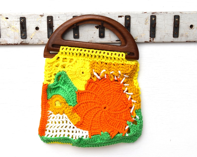 Pu&ograve; includere: Una borsa all'uncinetto fatta a mano, colorata, con manico in legno. La borsa presenta un design patchwork in giallo, arancione, verde e bianco. Il motivo floreale e il design unico la rendono un accessorio eccezionale.