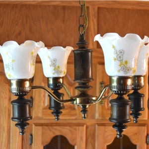 May include: A five-light chandelier with a brass finish and white glass shades. The shades feature a floral pattern with yellow and white flowers.