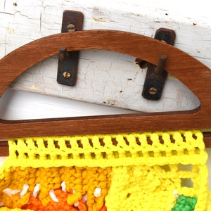 Pu&ograve; includere: Un telaio per borsa in legno con una parte superiore semicircolare e una base rettangolare, che contiene una borsa all'uncinetto colorata. La borsa presenta sezioni gialle, arancioni e verdi. Il telaio ha una piccola etichetta che dice "made in the Philippines".