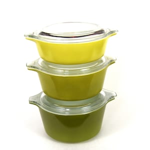 Może przedstawiać: Trzy vintage naczynia do zapiekania Pyrex ułożone jedno na drugim. Górne naczynie jest żółte, środkowe naczynie jest zielone, a dolne naczynie jest ciemnozielone.