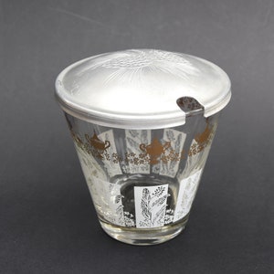 Puede incluir: Un azucarero de vidrio con tapa de plata y diseño floral dorado y blanco. La tapa tiene un pequeño pico para verter.