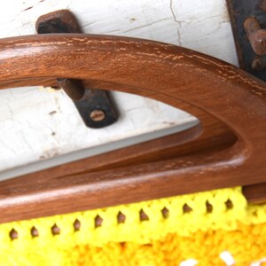 Pu&ograve; includere: Primo piano di un manico di borsa vintage in legno. Il manico &egrave; di colore marrone scuro e ha un design curvo e arcuato. Il tessuto all'uncinetto giallo e bianco della borsa &egrave; visibile sotto.
