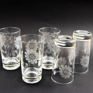 May include: Set of five clear glass tumblers with an etched floral design. The glasses are all the same size and shape, and they have a slightly rounded bottom.