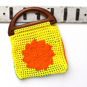 Pu&ograve; includere: Borsa all'uncinetto gialla con manico in legno e motivo floreale arancione. La borsa ha bordi verdi e arancioni. Il manico in legno &egrave; curvo e la borsa &egrave; fatta a mano.