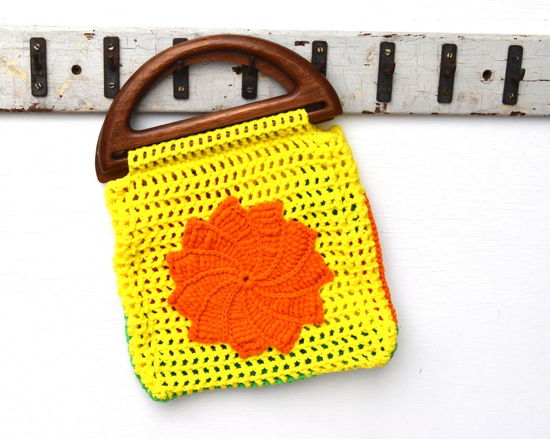 Pu&ograve; includere: Borsa all'uncinetto gialla con manico in legno e motivo floreale arancione. La borsa ha bordi verdi e arancioni. Il manico in legno &egrave; curvo e la borsa &egrave; fatta a mano.