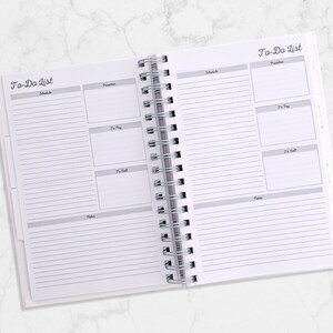 May include: Open white spiral-bound planner with "To-Do List" printed at the top of each page. The planner pages are divided into sections for scheduling, priorities, to-pay, to-call, and notes. The pages are lined with gray lines.