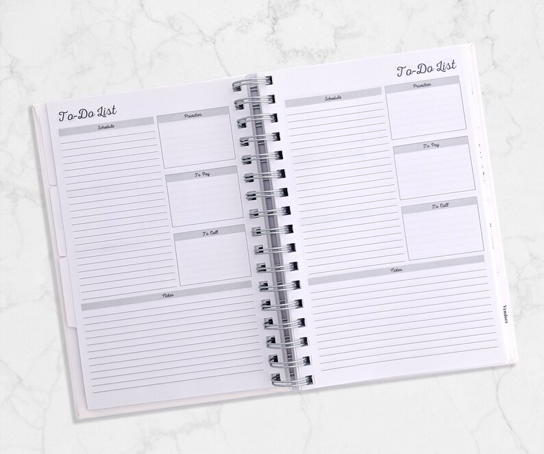 May include: Open white spiral-bound planner with "To-Do List" printed at the top of each page. The planner pages are divided into sections for scheduling, priorities, to-pay, to-call, and notes. The pages are lined with gray lines.