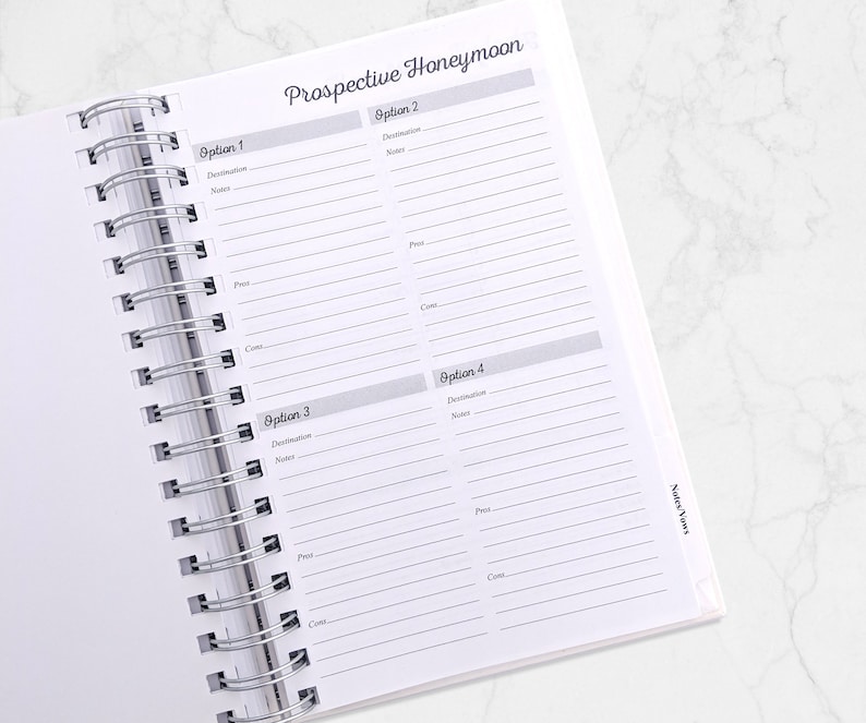 May include: Open spiral-bound notebook with a page titled "Prospective Honeymoon." The page is divided into sections for comparing options, with spaces for destination, notes, pros, and cons. The notebook is white with gray text.