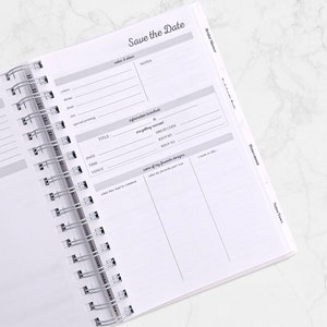 May include: Open planner with a silver spiral binding. The pages are white with gray text and lines. The top right corner reads "Save the Date". Sections include "Bridal Shower" and "Honeymoon".