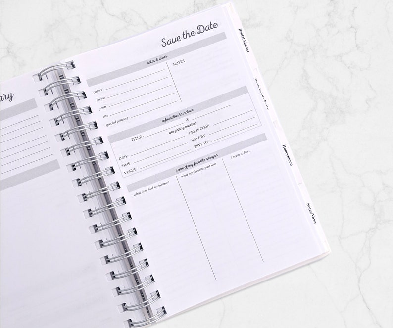 May include: Open planner with a silver spiral binding. The pages are white with gray text and lines. The top right corner reads "Save the Date". Sections include "Bridal Shower" and "Honeymoon".