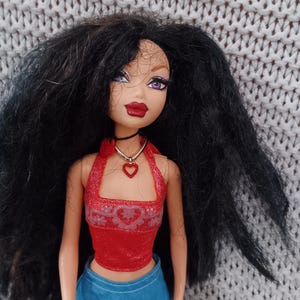 May include: A black-haired doll with purple eyeshadow and red lipstick wearing a red halter top with a heart design and a blue denim skirt.