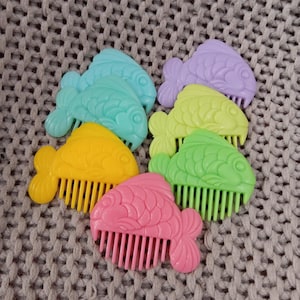 May include: Set of seven colorful plastic fish-shaped hair combs. The combs are in shades of blue, green, yellow, pink, and purple.