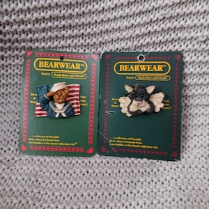 May include: Two Bearwear pins on green cards. One pin features a teddy bear in a sailor uniform with an American flag. The other pin shows a black and white bear with wings. The cards read "Bearwear from Boyd's Bears and Friends."