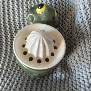 以下が含まれることがあります： 黄色の目をしたカエルの形をした緑色のセラミック製の柑橘類ジューサー。ジューサーは、星型の絞り器と縁の周りに穴のある白いセラミック製のトップを持っています。