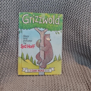 Puede incluir: Un libro infantil titulado "Grizzwold" con una portada verde y amarilla. La portada presenta un oso pardo abrazando un árbol, con el texto "Story and pictures by Syd Hoff" y "An I CAN READ Book."