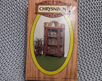 May include: A brown wooden dollhouse miniature kit of a corner cabinet with glass doors and shelves. The box has the text "CHRYSNBON" and "MODEL KIT F-120" printed on it.