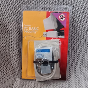 May include: A Qualtec PC BASIC Security kit in a clear plastic package. The packaging is orange and red with a computer graphic. The kit includes a silver padlock, keys, a cable, and an alcohol prep pad.
