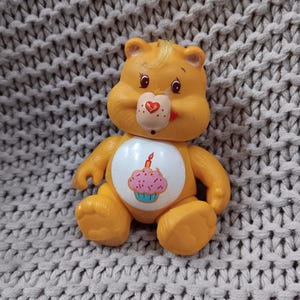 Vintage poseable 4-inch orange Care Bear figurine with rooted hair and Cupcake on their tummy c. 1983 - Birthday Bear