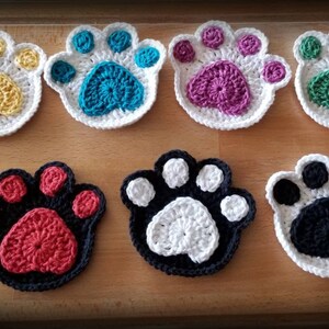 May include: Seven crocheted paw print coasters in various colors, including yellow, teal, purple, green, red, white, and black.