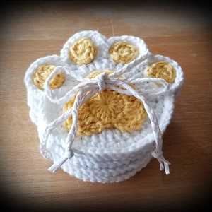 May include: Set of four crocheted white paw print coasters with yellow centers. The coasters are tied together with a white string.