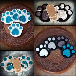 May include: Set of crocheted paw print coasters in various colors, including white, gray, black, and blue. The coasters are handmade and feature a tag that reads "Handmade with love by Paw & Co."