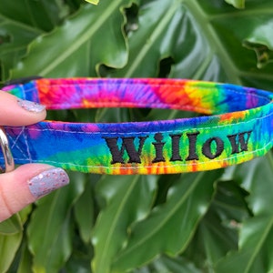 May include: A colorful dog collar with a tie-dye pattern in shades of blue, purple, yellow, and red. The name "Willow" is embroidered in black thread. The collar has a silver metal loop for attaching a leash.