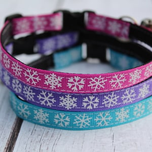 May include: Three cat collars with a snowflake pattern. The collars are pink, purple, and blue.