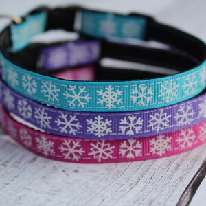 May include: Three cat collars with snowflake patterns. The collars are turquoise, purple, and pink with white snowflakes. The collars are made of ribbon and have a black adjustable strap.