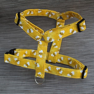 May include: Yellow dog harness with a bee pattern. The harness has black buckles and a silver D-ring.