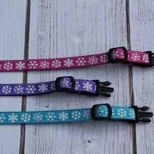 May include: Three adjustable dog collars with snowflake patterns. The collars are pink, purple, and blue with white snowflakes.