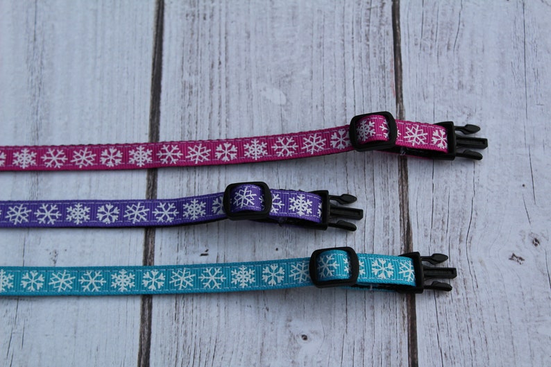 May include: Three adjustable dog collars with snowflake patterns. The collars are pink, purple, and blue with white snowflakes.