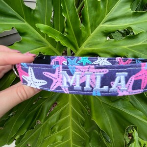May include: A dark blue dog collar with a pink and white starfish pattern and the name "Mila" embroidered in white.