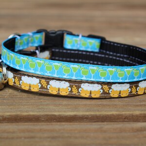 Op de afbeelding: Een bruin en blauwe kattenhalsband met een bel. De bruine halsband heeft een patroon van bierglazen en de blauwe halsband heeft een patroon van groene cocktailglazen.