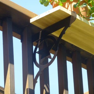 May include: A black metal shelf bracket with a decorative star design is attached to a wooden deck railing. The bracket supports a wooden shelf.