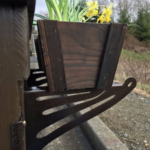 May include: A wooden planter box with yellow flowers is mounted on a brown metal bracket. The bracket is attached to a wooden surface.