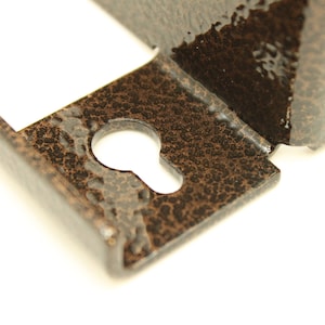 May include: Close-up of a metal keyhole cover with a textured, brown finish. The keyhole is visible in the centre of the cover.