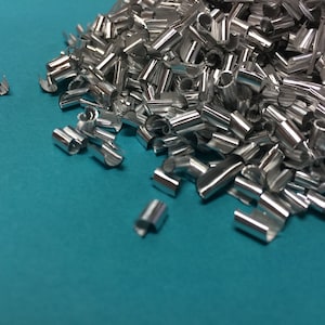 May include: A pile of silver metallic confetti, scattered on a turquoise blue surface.