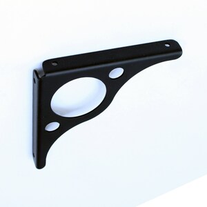 May include: Black metal shelf bracket with four holes. The bracket is angled and has a rounded edge.