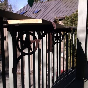May include: A black metal railing with a wooden top and star-shaped accents. The railing is attached to a wooden deck and a house in the background.