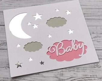 May include: White card with a pink cloud cutout that says "Baby" in white script. The card is decorated with silver stars and a silver crescent moon.