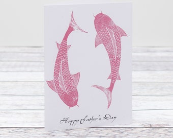 May include: A pink greeting card with two pink fish printed on it. The card says "Happy Father's Day".