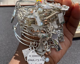 May include: A silver charm bracelet with multiple charms, including a charm with the text "A Sister is someone you dream, cry, sing, laugh with".