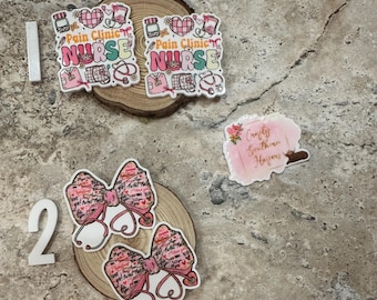 May include: A collection of nurse-themed accessories, including two rectangular badges with the text "Pain Clinic Nurse" and a heart design, and two bow-shaped badges with stethoscope details. The badges are on a wooden slice.