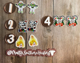 May include: Assorted decorative charms and numbers on a wooden surface. Includes Buzz Lightyear, the text "You've Got A Friend In Me", and Christmas-themed designs. The numbers 1, 2, 3, and 4 are also present, along with the text "@Crafty Southern Heifers".